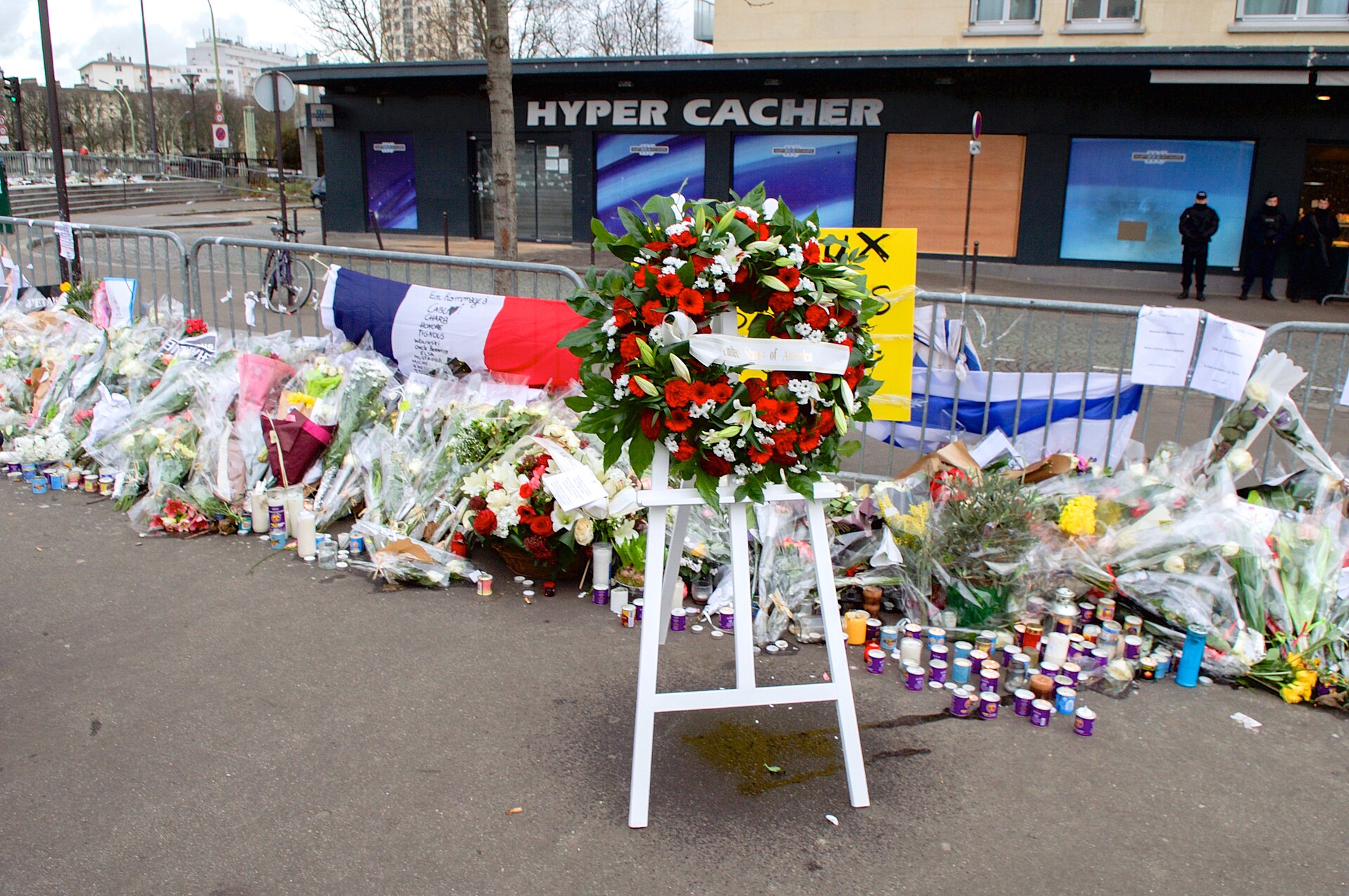 Wieńce złożone przed sklepem Hyper Cacher w Paryżu ku pamięci ofiar zamachu ze stycznia 2015 roku. Źródło: Wikimedia Commons — The Wreath Laid by Secretary Kerry and French Foreign Minister Fabius Is Pictured Outside the Hyper Cacher Kosher Market in Paris (16106400057).